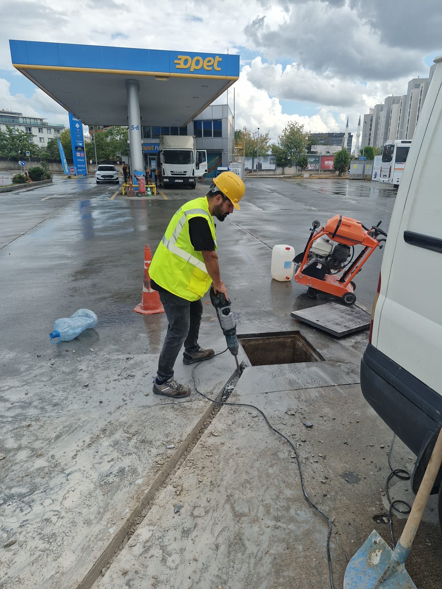 Açık şarj sahasında beton kesme makinesiyle çalışan reflektörlü yelekli usta