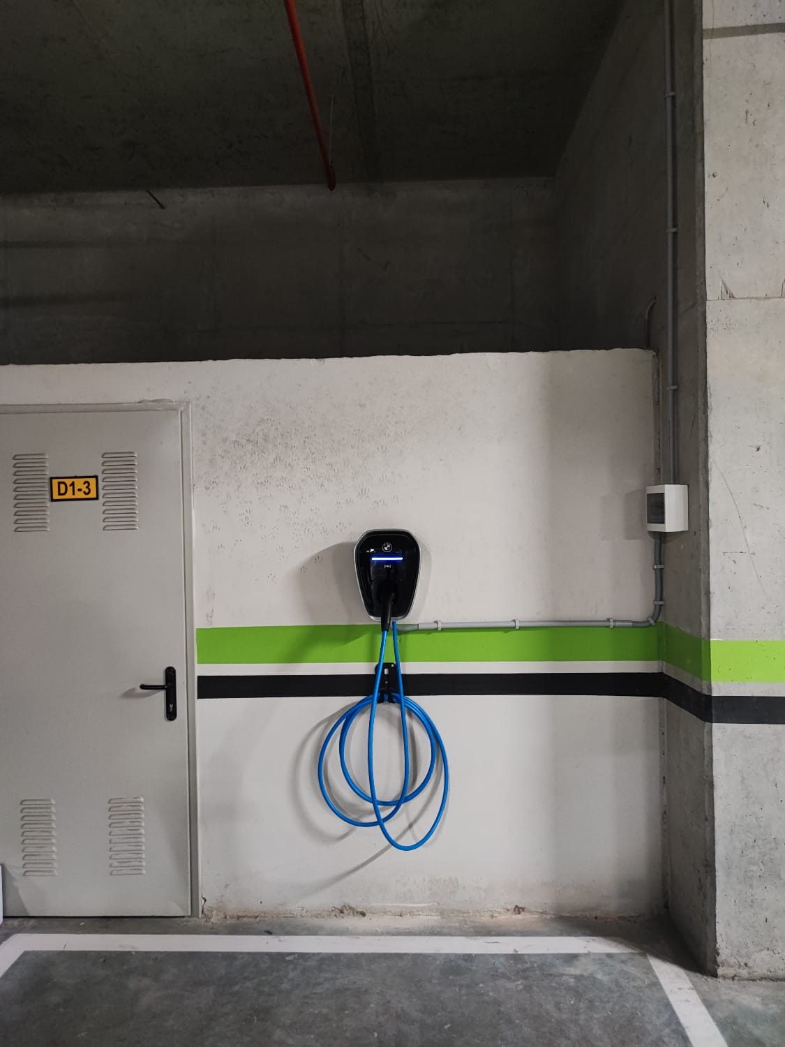 Konut otoparkı duvarına monte edilmiş, kablosu askıda AC şarj cihazı